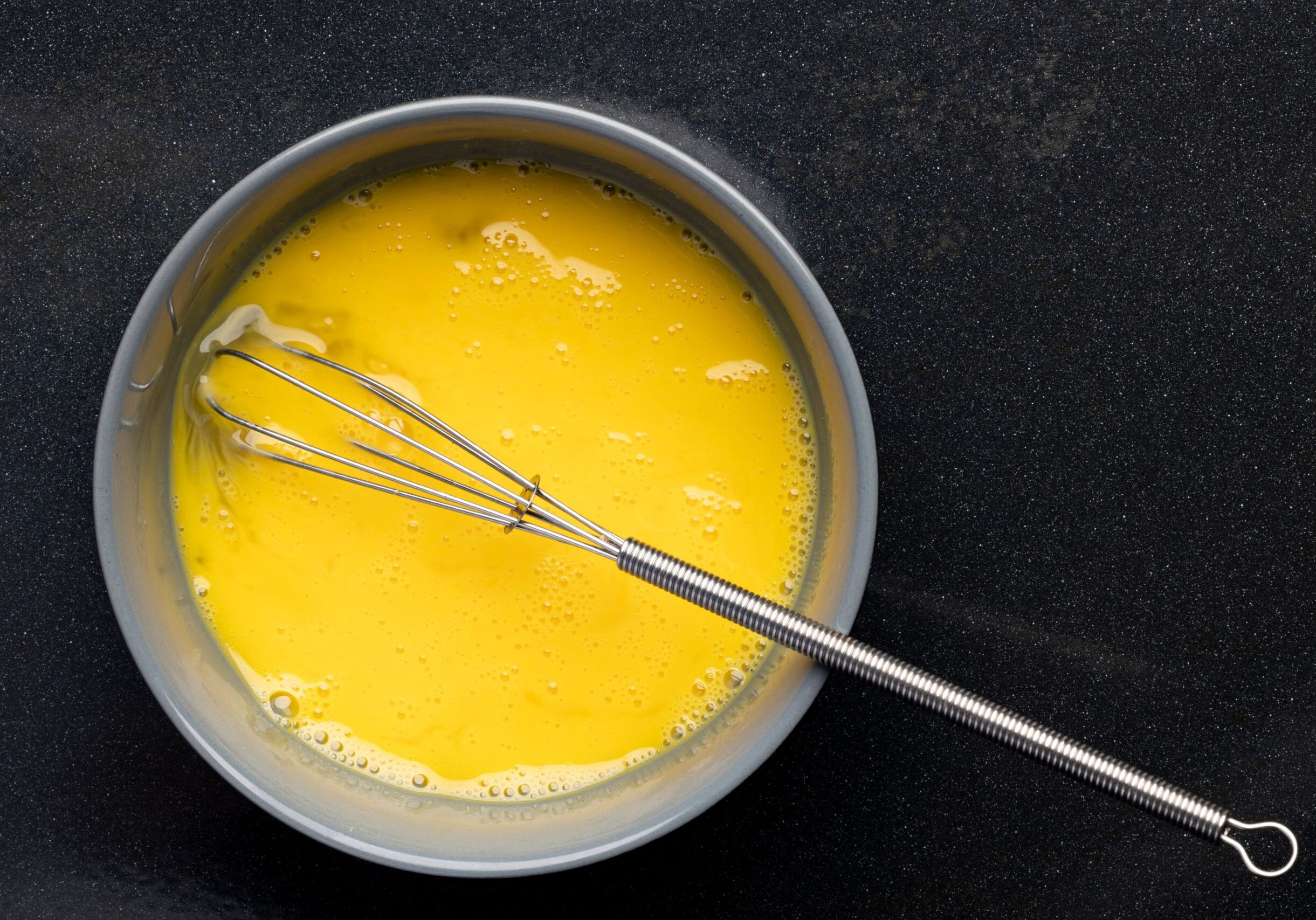 A closeup of beaten eggs in a bowl with a whisk